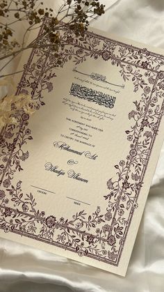 an ornate wedding card with arabic writing on it and flowers in the foreground next to it