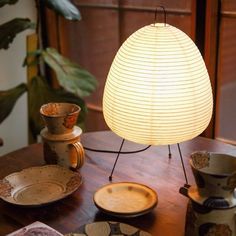 a lamp sitting on top of a wooden table next to plates and cups in front of it