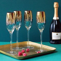 three wine glasses on a tray with raspberries in front of a bottle of champagne