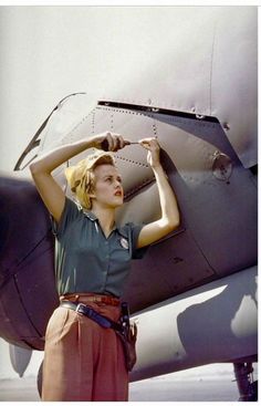 a woman standing in front of an airplane with her hands on the side of it