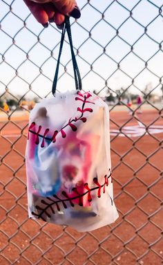 a hand holding a bag with baseballs on it hanging from a chain link fence