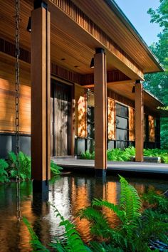 a house that is next to some water and plants in front of the house,