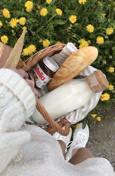 a basket filled with bread, milk and other items next to some yellow dandelions