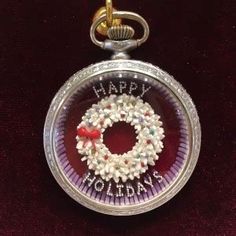 a small pocket watch with a wreath on the front and happy holidays written on it