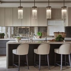 a kitchen island with four stools in front of it and lights hanging from the ceiling