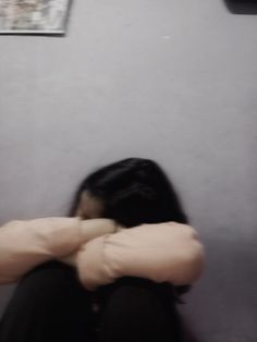 a woman sitting on the floor with her arms folded over her head and looking down