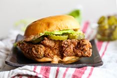 a fried chicken sandwich with pickles and jalapenos on a black plate