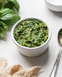 a white bowl filled with green pesto next to two spoons on top of a table