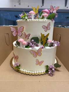 a three tiered cake decorated with butterflies and flowers on top of a cardboard box