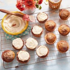 cupcakes with icing on a cooling rack next to a bowl of whipped cream