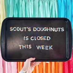 a person holding up a sign that says scout's doughnuts is closed this week