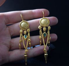 This 22 Karat Gold Emerald pair of earrings is inspired by ancient greek and Byzantine Jewelry. Handmade with love and craftsmanship, adorned with daisies, hand-wonen chain and 0.8 ct emeralds. Definitely a statement, this unique pair will steal the spotlight and everyones heart. In Ancient Greece, daisies were a symbol of purity, simplicity, and transformation. Daisies are composite flowers, meaning that they actually consist of two flowers combined into one. For that reason they symbolize true Greek Earrings Ancient, Historical Earrings, Ancient Greece Jewelry, Ancient Greek Jewelry, Byzantine Jewelry, 22k Gold Earrings, Faberge Jewelry, Greek Gifts, Jewelry Designing