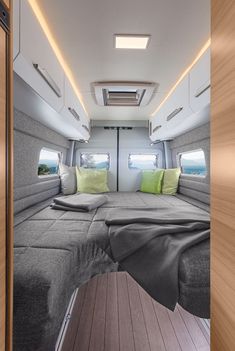 the interior of a camper with wood flooring and green pillows on the bed