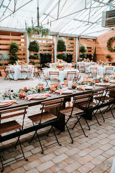 a long table set up with plates and place settings for an outdoor wedding reception in a greenhouse