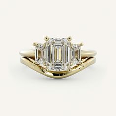 an emerald cut diamond ring with three side stones in yellow gold, on a white background