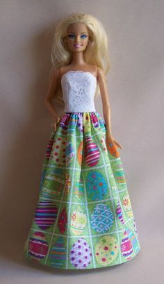 a barbie doll wearing a colorful dress with white top and green skirt, standing on a pink background