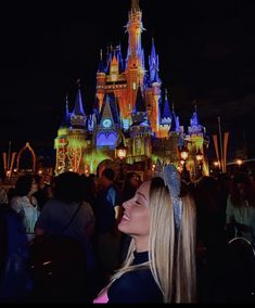 a woman standing in front of a castle at night with lights on it's side