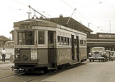 an old photo of a trolley car on the tracks in front of a building with cars parked nearby