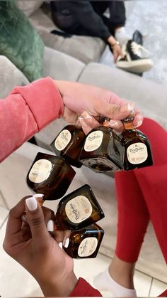 two women are holding up bottles of liquor in their hands while another woman sits on the couch