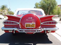 the back end of a red classic car parked in a parking lot next to other cars