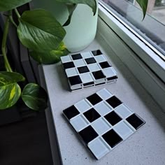 two black and white tiles sitting on top of a window sill next to a potted plant