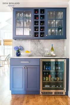 a kitchen with blue cabinets and wine glasses on the glass doored cabinet above it