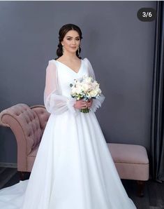 a woman in a white wedding dress standing next to a couch