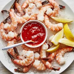 a white plate topped with shrimp next to lemon wedges and ketchup sauce