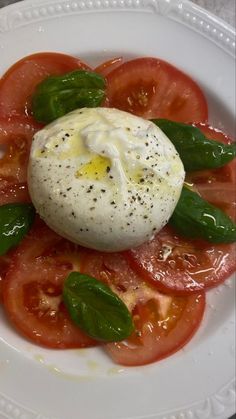 a white plate topped with sliced tomatoes and an egg on top of basil leafy greens