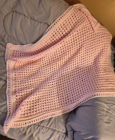 a pink crocheted blanket laying on top of a bed