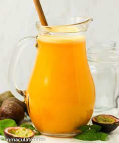 a glass pitcher filled with orange juice next to some figs and other fruit on the table