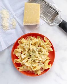 a red plate topped with pasta and cheese next to a grater on a counter