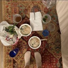 two bowls of noodles and chopsticks are on the floor next to someone's feet