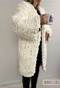 a woman is holding a coffee cup and wearing a white knitted coat