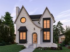 a white and black house with two windows on the front, surrounded by greenery