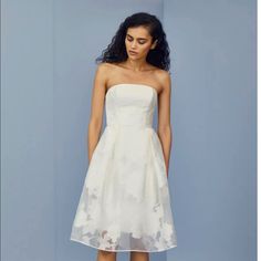 a woman standing in front of a blue wall wearing a white dress with flowers on it