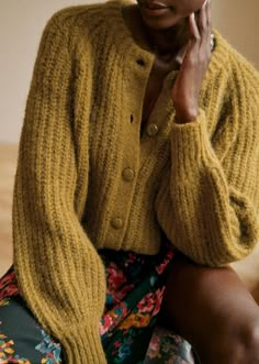 a woman in a yellow cardigan sitting on a chair with her hand under her chin