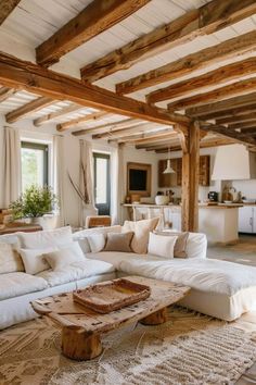 a living room filled with lots of white furniture and wooden beamed ceiling beams in an open floor plan