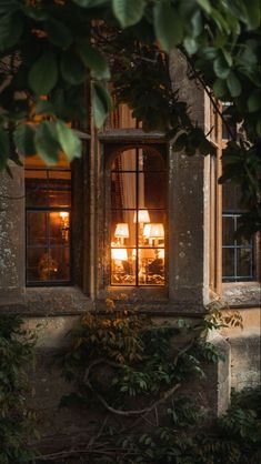 two lamps are lit in the window of an old building with ivy growing around it