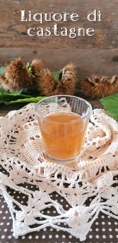 a glass cup filled with liquid sitting on top of a doily next to leaves