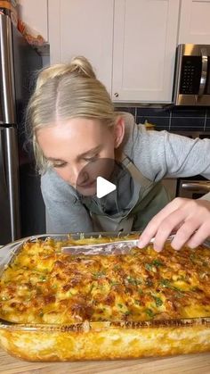 a woman is looking at a casserole in the kitchen with her hands on it