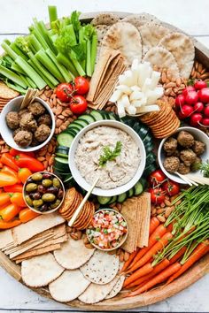 a platter filled with vegetables, crackers and dips on top of it