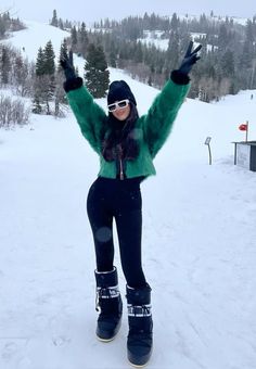 a woman standing on top of a snow covered slope wearing skis and holding her arms in the air