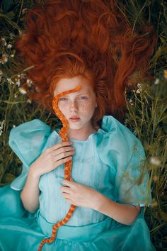 a woman with red hair laying on the ground holding an orange object in front of her face