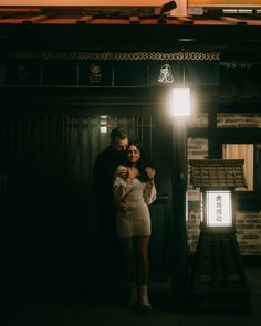 a man and woman standing next to each other in front of a building at night