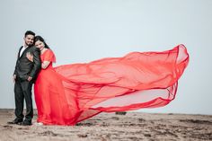 a man and woman are standing in the desert with an orange dress blowing in the wind