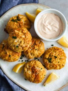 baked crab cakes on a white plate with lemon wedges and dip in the middle