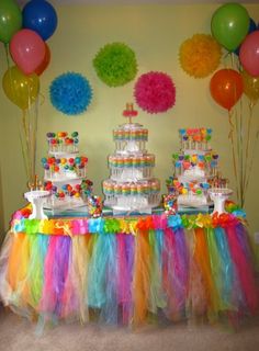 a table topped with lots of cake next to balloons and paper pom poms