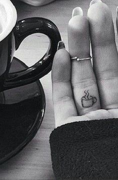 two fingers that have tattoos on them next to a cup and saucer with coffee in it