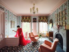 a woman in a red dress sitting on a bathtub next to two chairs and a fireplace